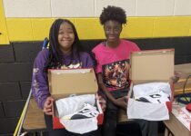 two young female athletes showing open boxes of Nike basketball shoes